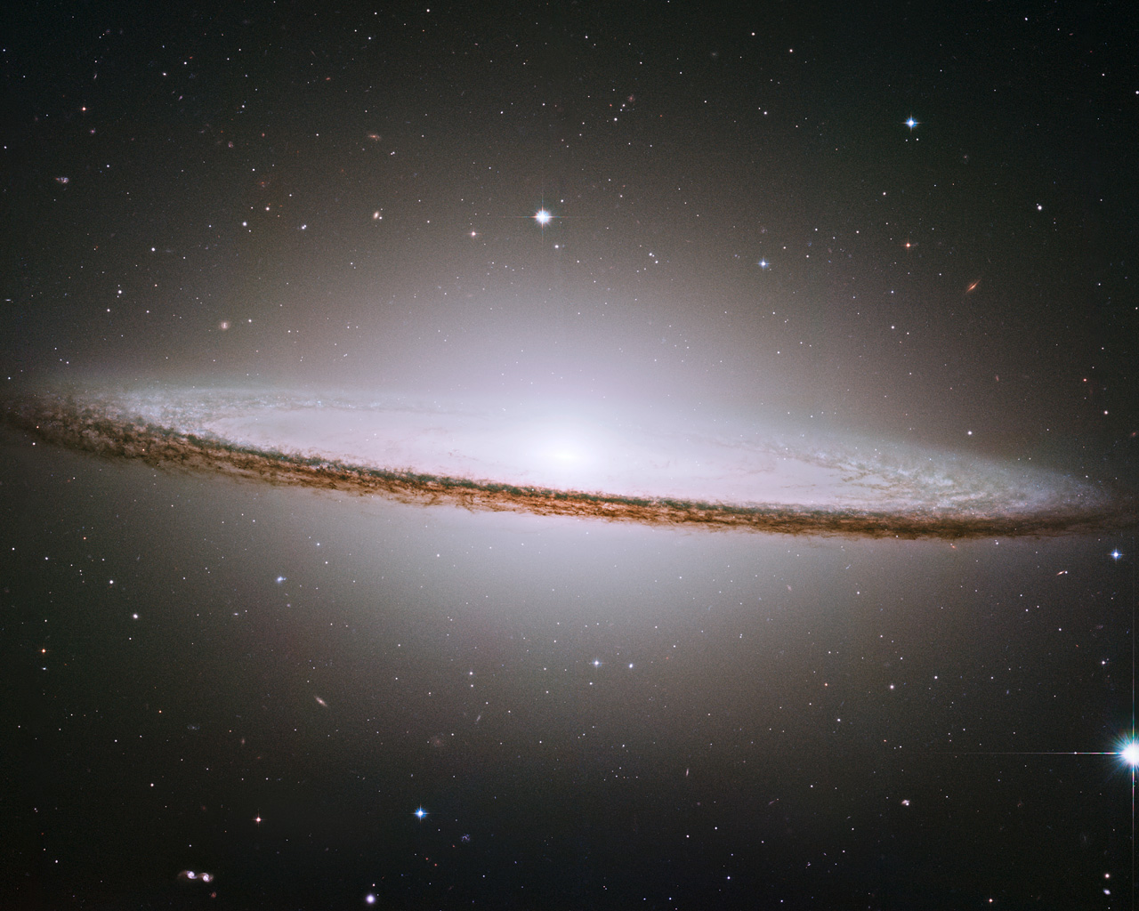 NASA/ESA Hubble Space Telescope has trained its razor-sharp eye on one of the universe's most stately and photogenic galaxies, the Sombrero galaxy, Messier 104 (M104). The galaxy's hallmark is a brilliant white, bulbous core encircled by the thick dust lanes comprising the spiral structure of the galaxy. As seen from Earth, the galaxy is tilted nearly edge-on. We view it from just six degrees north of its equatorial plane. This brilliant galaxy was named the Sombrero because of its resemblance to the broad rim and high-topped Mexican hat. At a relatively bright magnitude of +8, M104 is just beyond the limit of naked-eye visibility and is easily seen through small telescopes. The Sombrero lies at the southern edge of the rich Virgo cluster of galaxies and is one of the most massive objects in that group, equivalent to 800 billion suns. The galaxy is 50,000 light-years across and is located 28 million light-years from Earth.